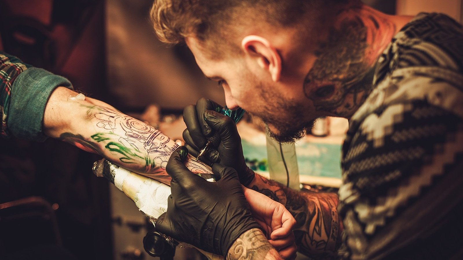 Tattoo artist makes a tattoo on a man's hand.